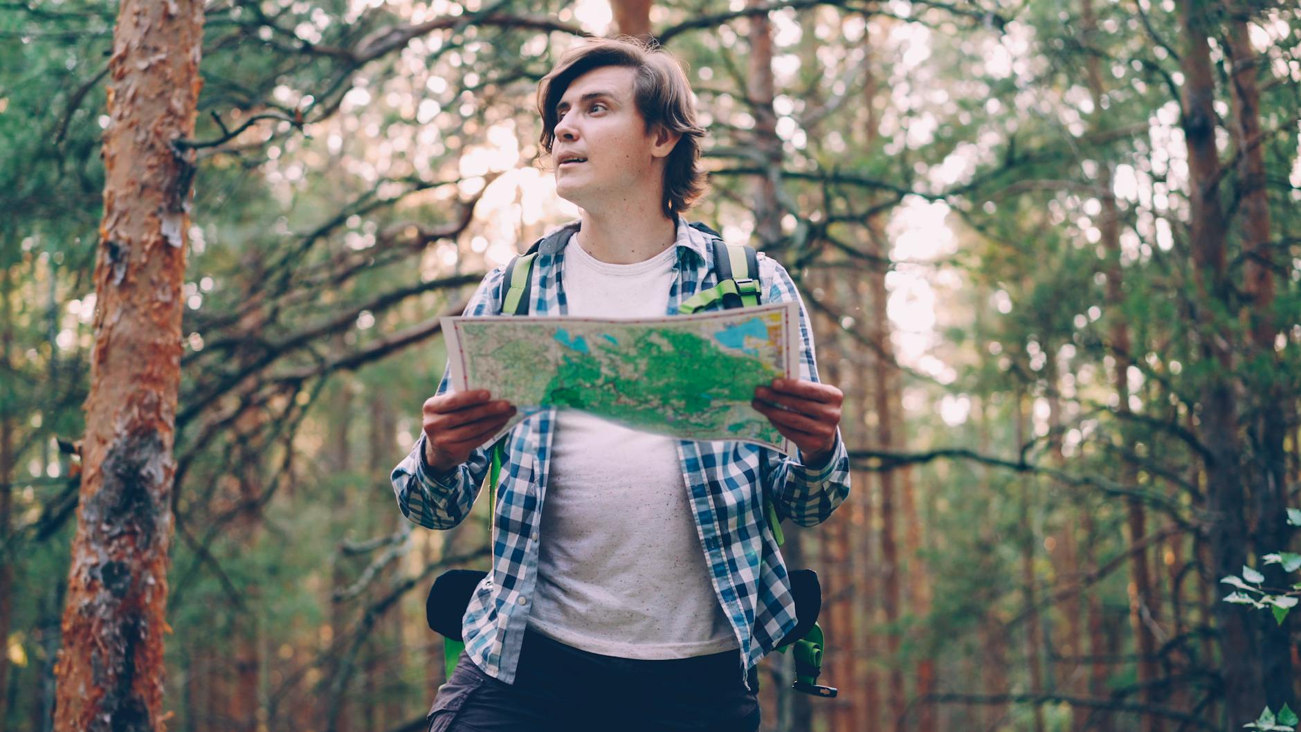 Mężczyzna w kraciastej koszuli czyta mapę podczas spaceru po lesie