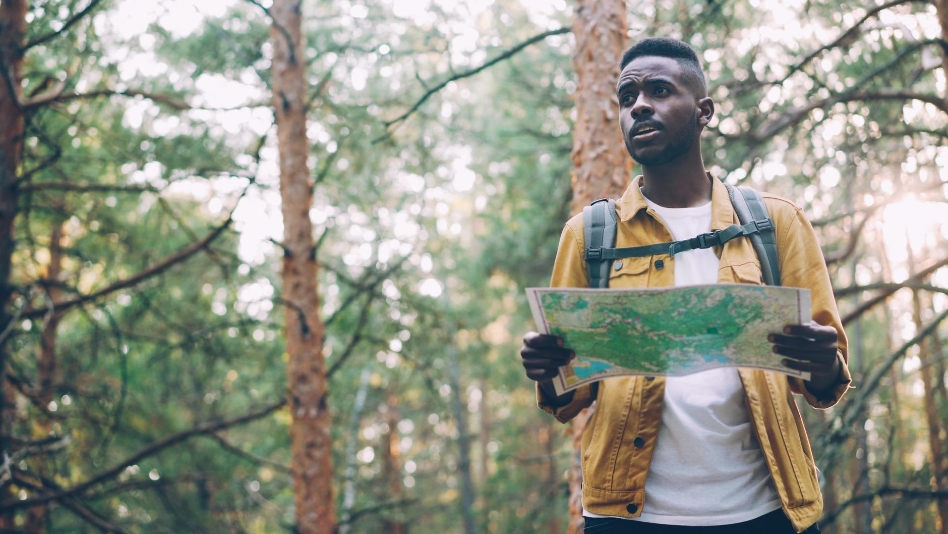 Młody mężczyzna z mapą i plecakiem idzie leśnym szlakiem