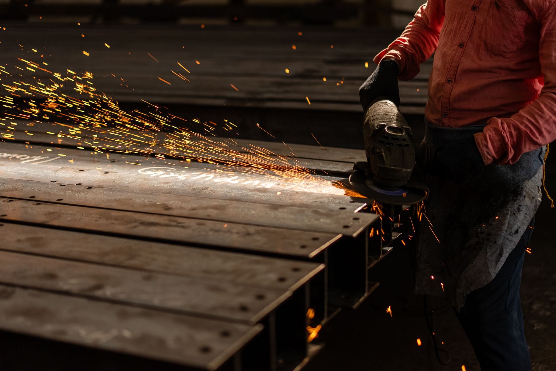 Pracownik szlifuje metalowe belki szlifierką kątową, lecą iskry