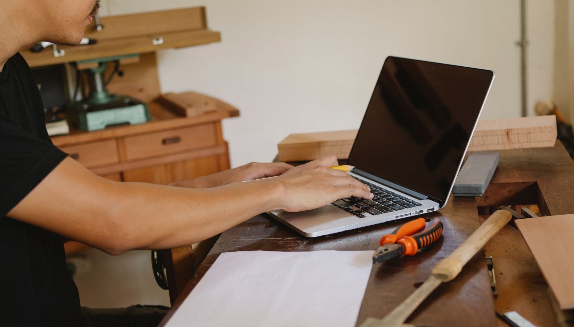 Mężczyzna w warsztacie przy stole z narzędziami pracuje na laptopie