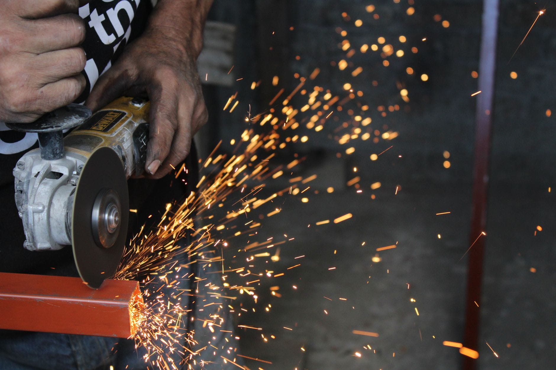 Pracownik tnie metal szlifierką kątową, iskry lecą w hali produkcyjnej Pracownik tnie metal szlifierką kątową, iskry lecą w hali produkcyjnej